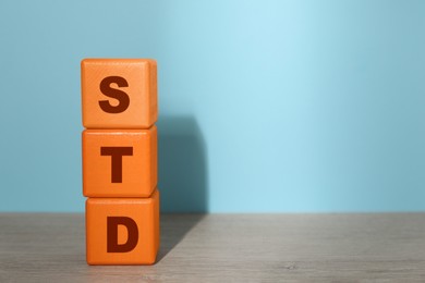 Abbreviation STD made with cubes on wooden table against light blue background, space for text