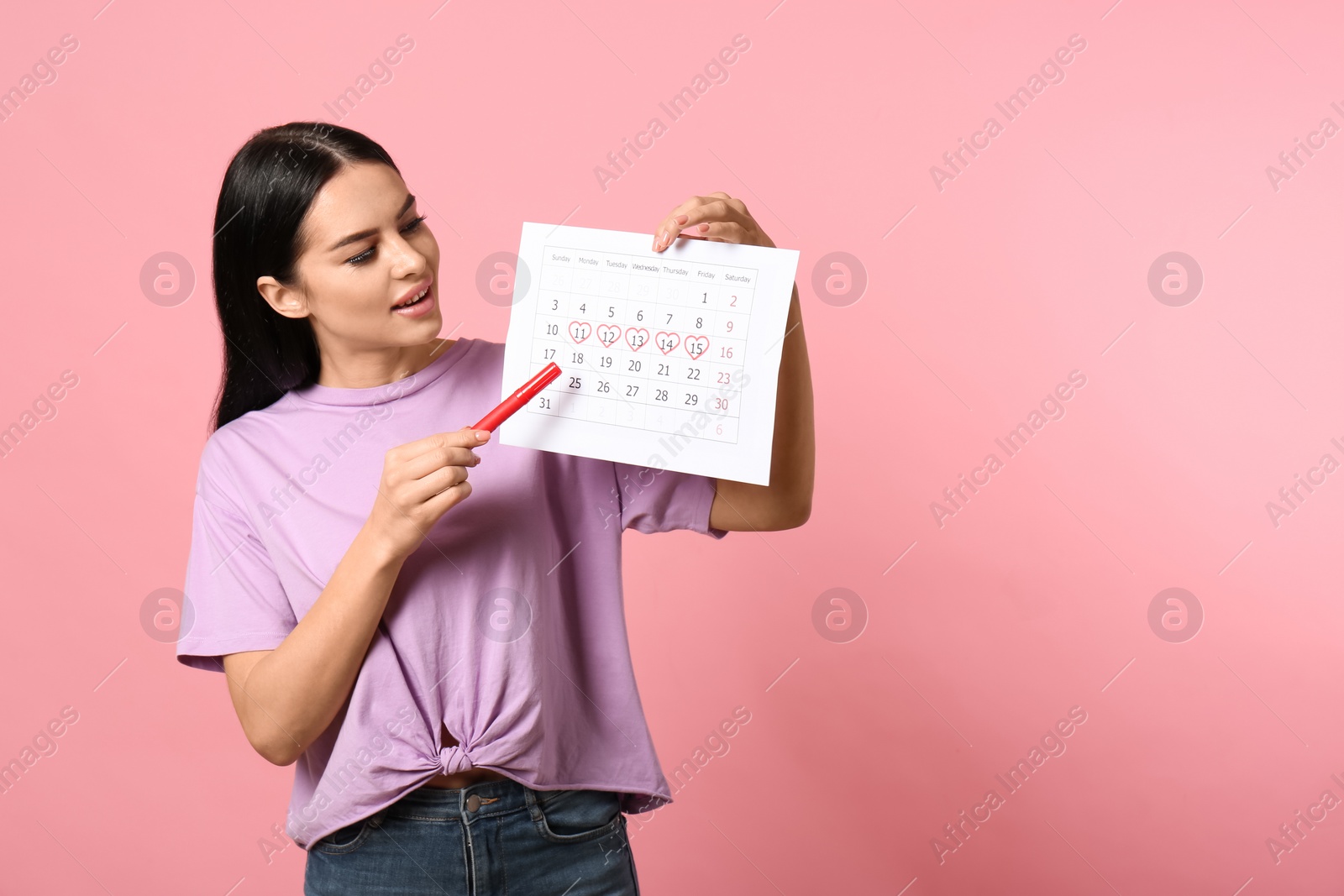 Photo of Young woman holding calendar with marked menstrual cycle days on pink background