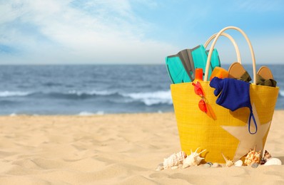 Bag with beach objects on sand near sea, space for text