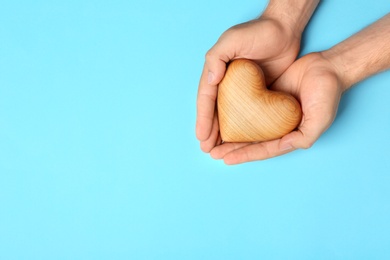 Young man holding wooden heart on light blue background, top view with space for text. Donation concept