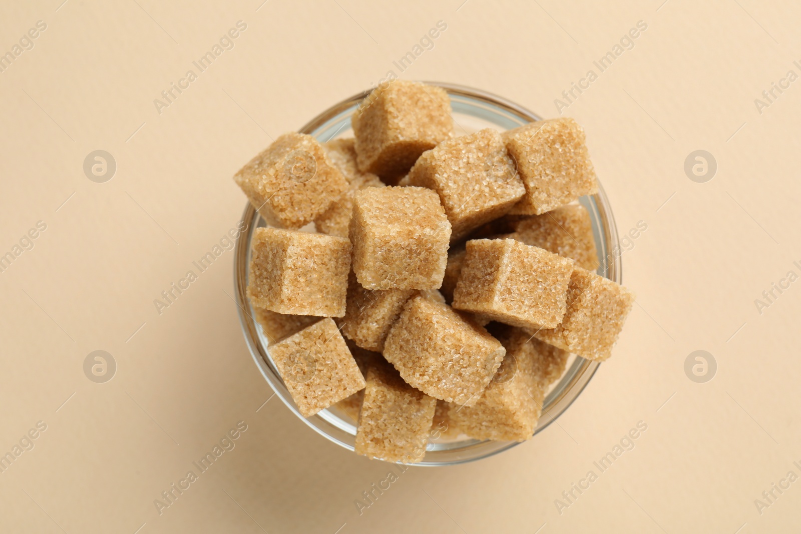 Photo of Brown sugar cubes in bowl on beige background, top view