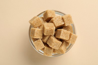 Brown sugar cubes in bowl on beige background, top view