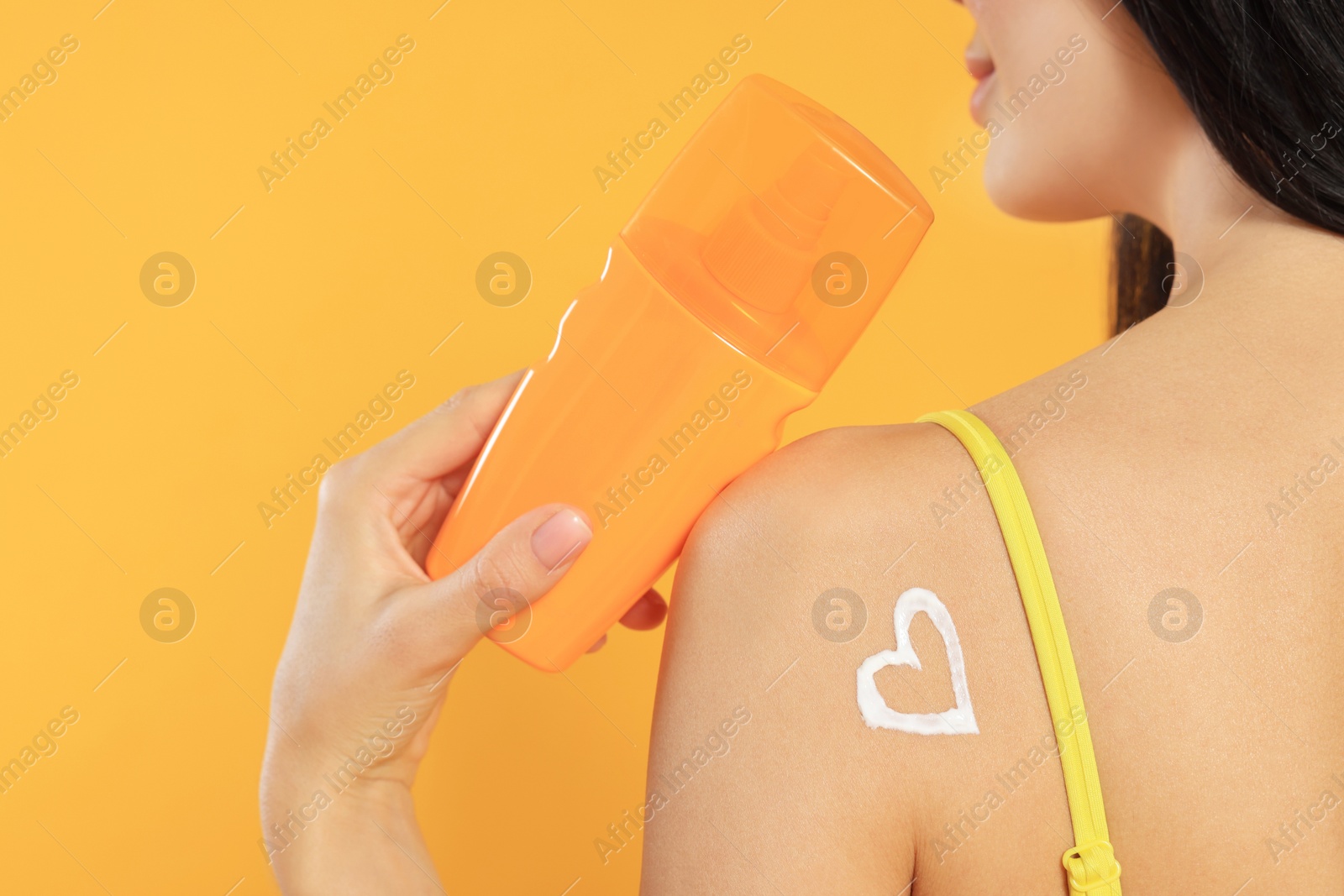 Photo of Young woman with heart drawn with sunscreen against orange background, closeup