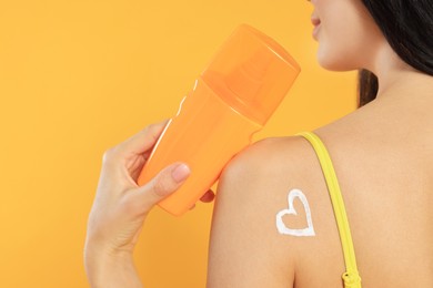 Photo of Young woman with heart drawn with sunscreen against orange background, closeup