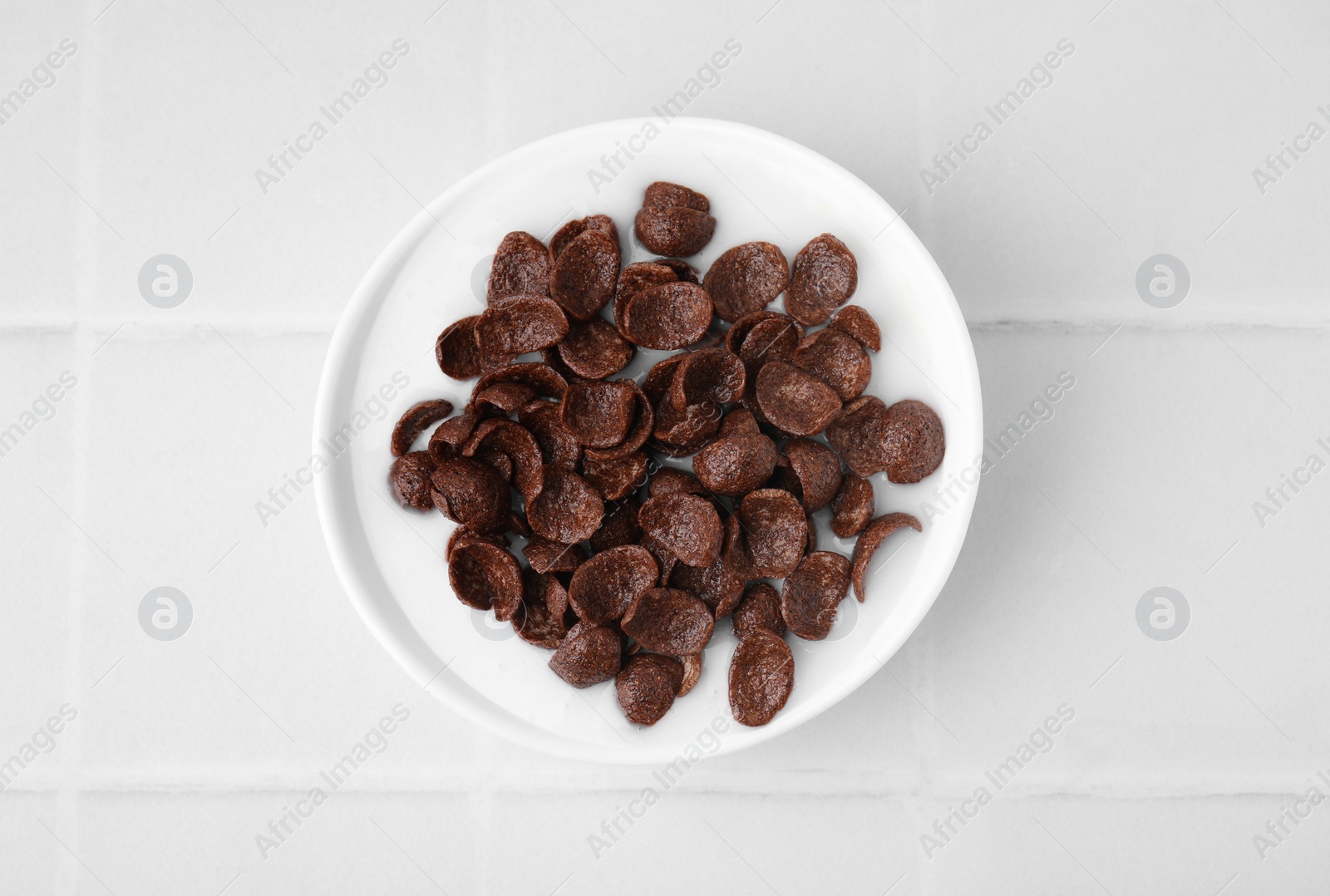 Photo of Breakfast cereal. Chocolate corn flakes and milk in bowl on white tiled table, top view