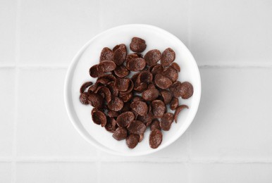 Photo of Breakfast cereal. Chocolate corn flakes and milk in bowl on white tiled table, top view