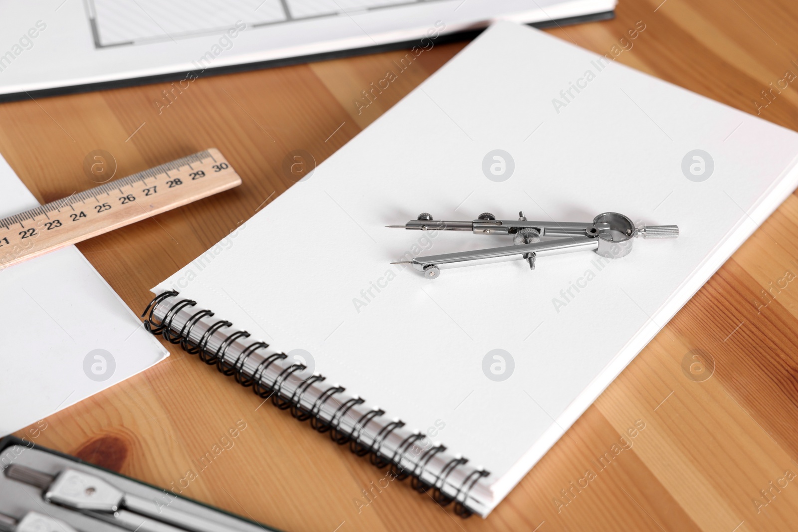 Photo of Sketchbook, pair of compasses and ruler on wooden table