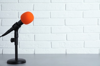 Modern microphone on table near brick wall. Space for text