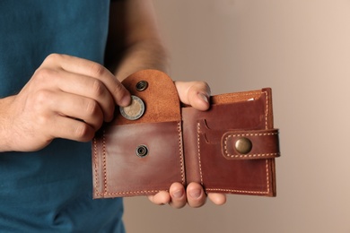 Photo of Young man putting coin into wallet on beige background, closeup