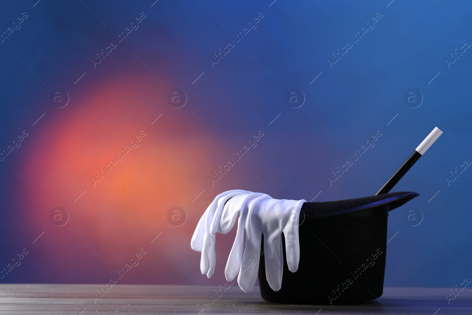 Photo of Magician's hat, wand and gloves on wooden table against color background, space for text