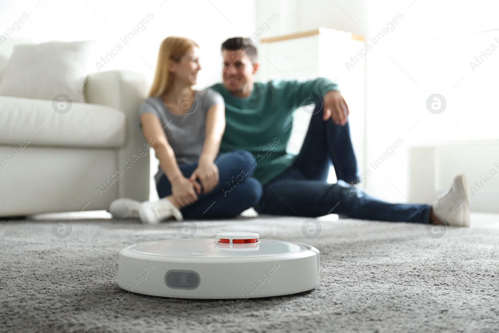 Photo of Couple spending time together while robotic vacuum cleaner doing its work at home