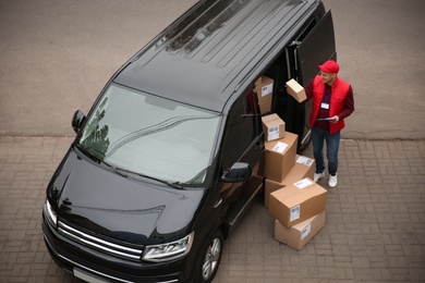 Photo of Courier with clipboard and parcels near delivery van outdoors, above view