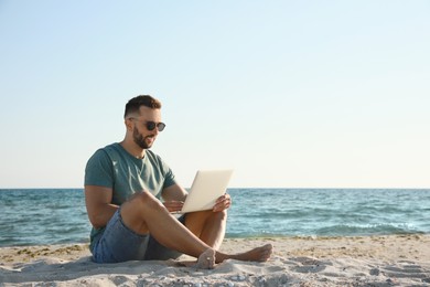 Photo of Man working with laptop on beach. Space for text