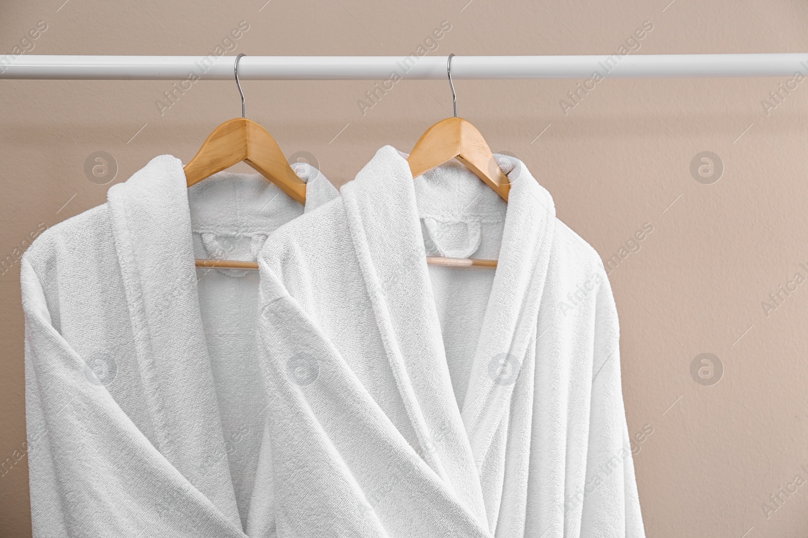 Photo of Fresh white bathrobes hanging on rack near beige wall