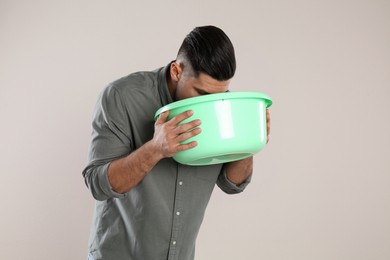 Man with basin suffering from nausea on beige background. Food poisoning