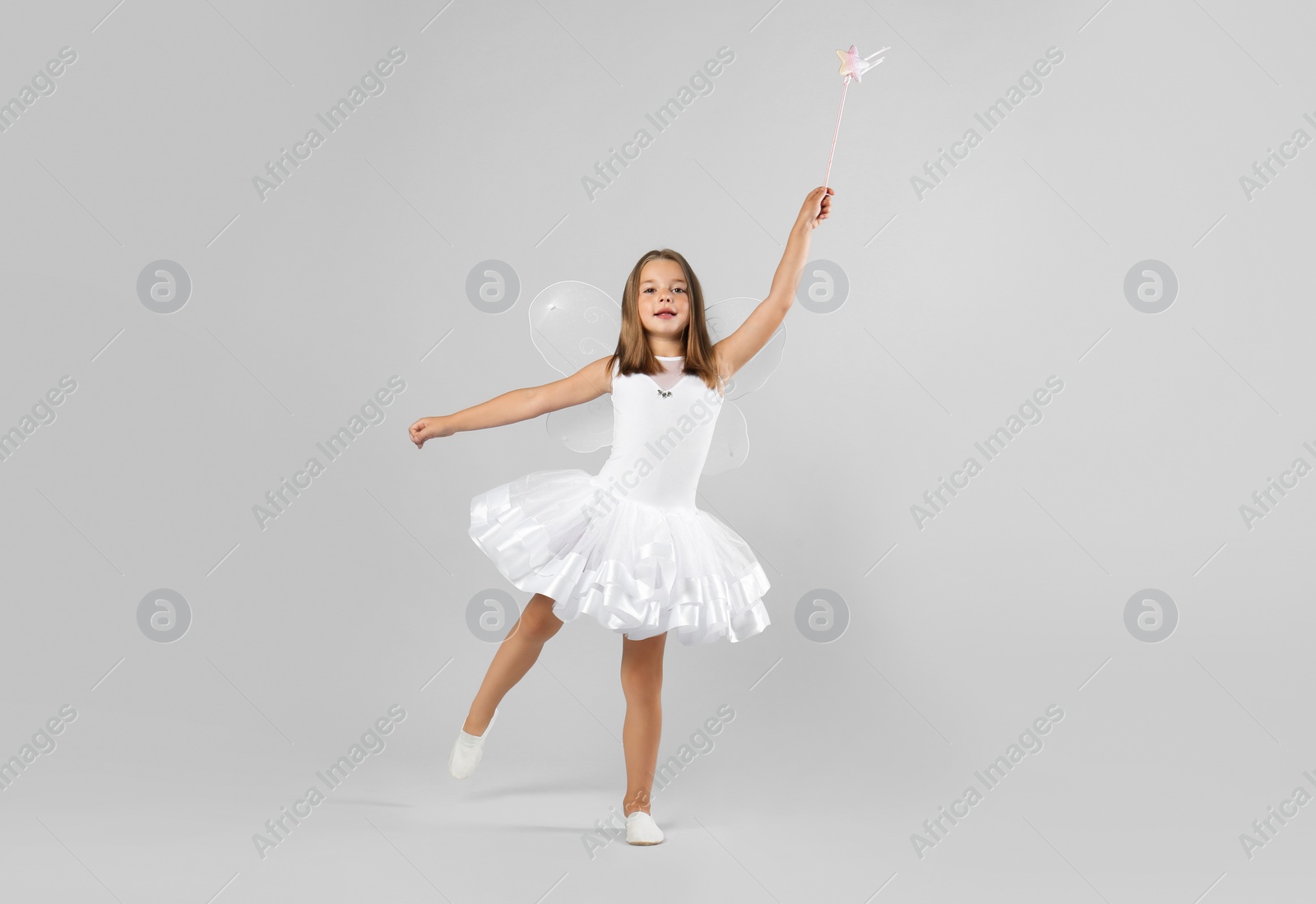 Photo of Cute little girl in fairy costume with wings and magic wand on light background. Space for text
