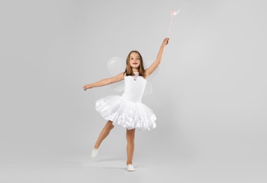 Photo of Cute little girl in fairy costume with wings and magic wand on light background. Space for text