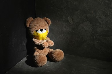 Photo of Stop child abuse. Tied toy bear with taped mouth in dark room. Space for text