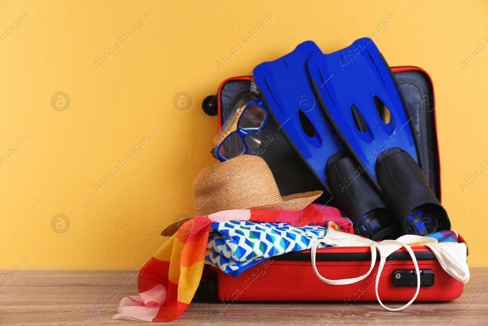 Photo of Open suitcase with clothing and swimming accessories on table. Space for text
