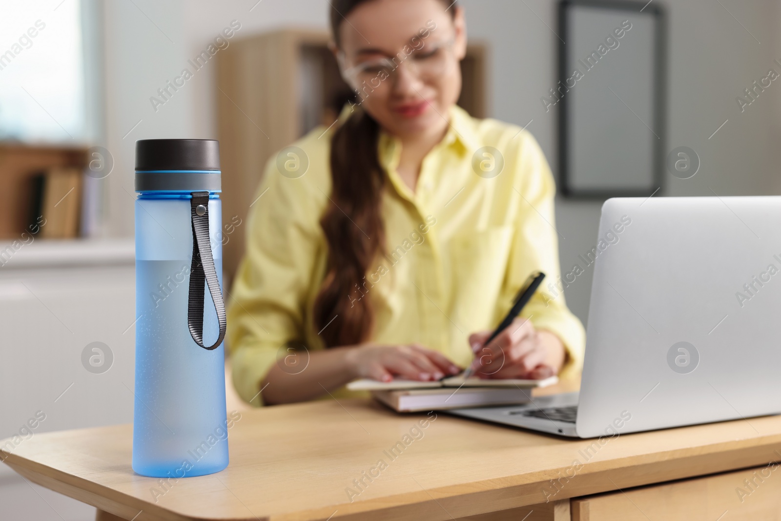 Photo of Woman working at wooden desk indoors, focus on bottle. Space for text
