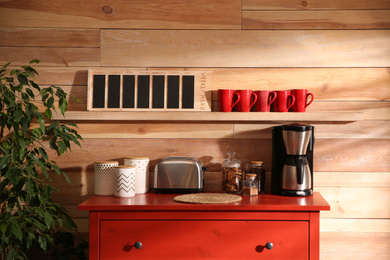 Photo of Stylish room interior with modern coffeemaker and toaster on red chest of drawers