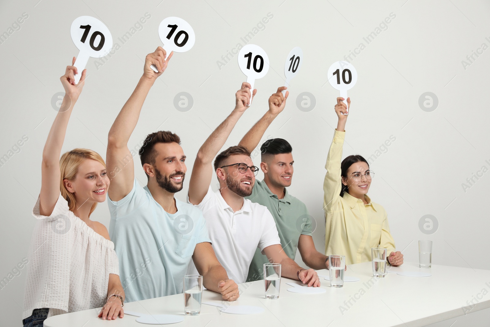 Photo of Panel of judges holding signs with highest score at table on white background