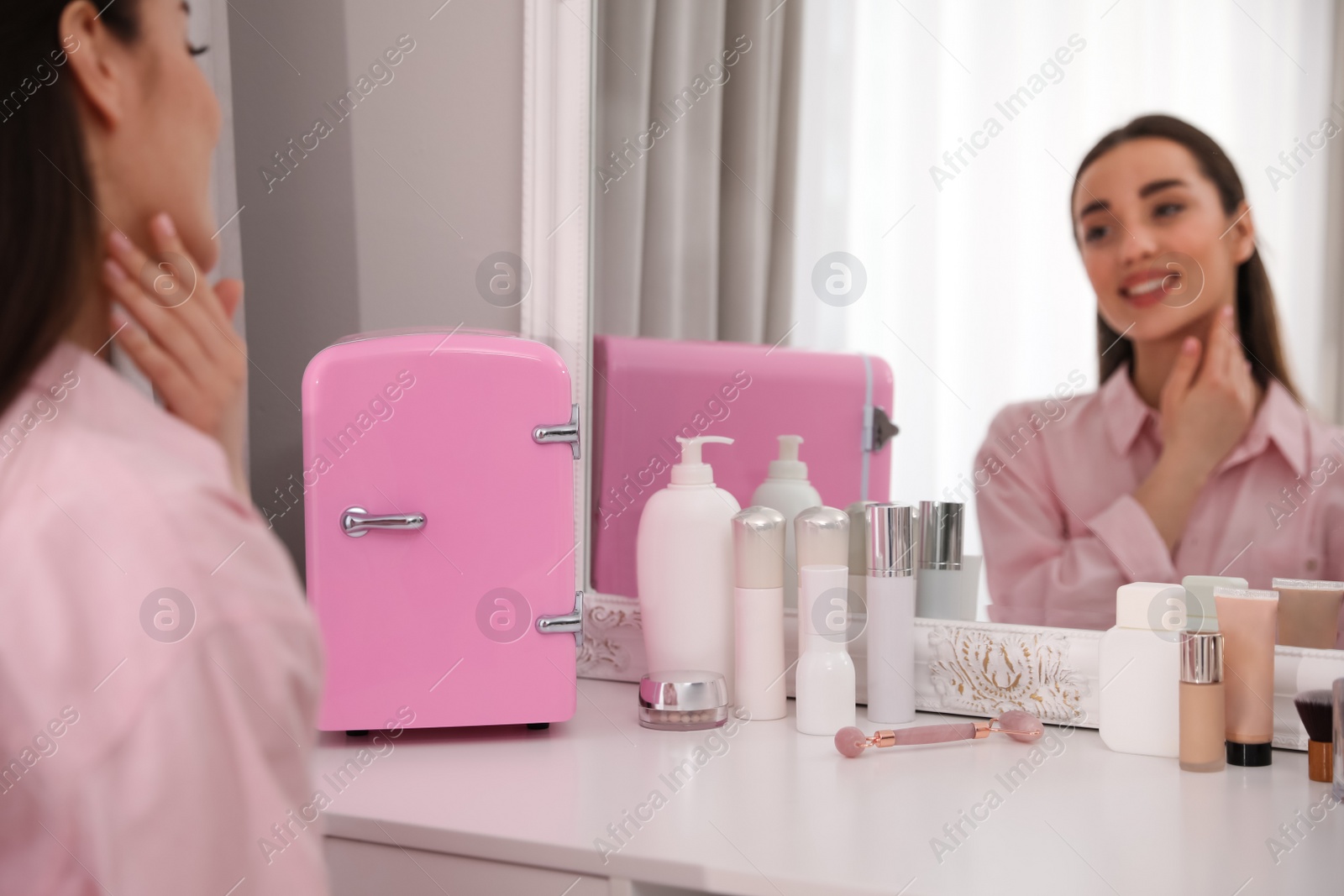 Photo of Woman getting ready at dressing table with cosmetic fridge indoors