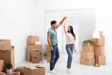 Photo of Happy couple dancing in room with cardboard boxes on moving day