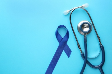 Blue awareness ribbon and stethoscope on color background, flat lay. Symbol of medical issues