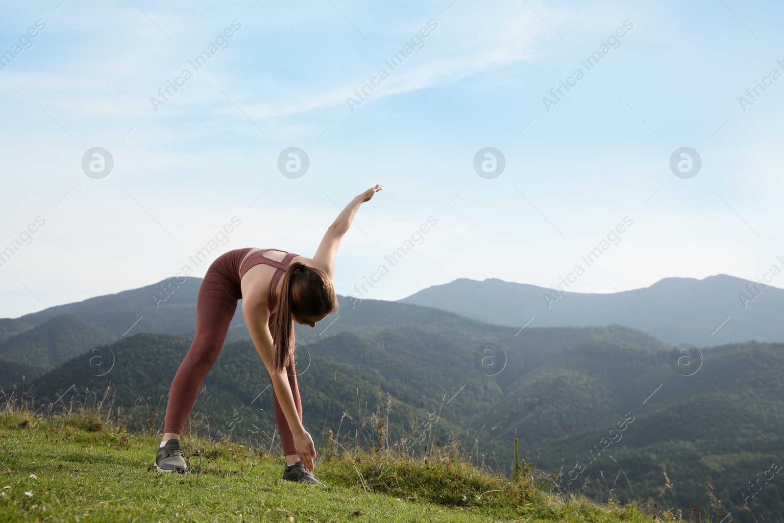 Photo of Young woman doing morning exercise in mountains, space for text