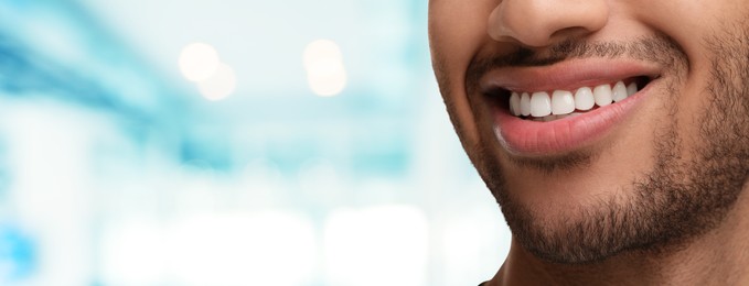 Man with clean teeth smiling on blurred background, closeup. Banner design with space for text