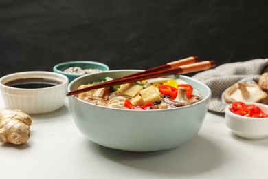 Photo of Bowl of delicious ramen, ingredients and chopsticks on white table, closeup. Noodle soup