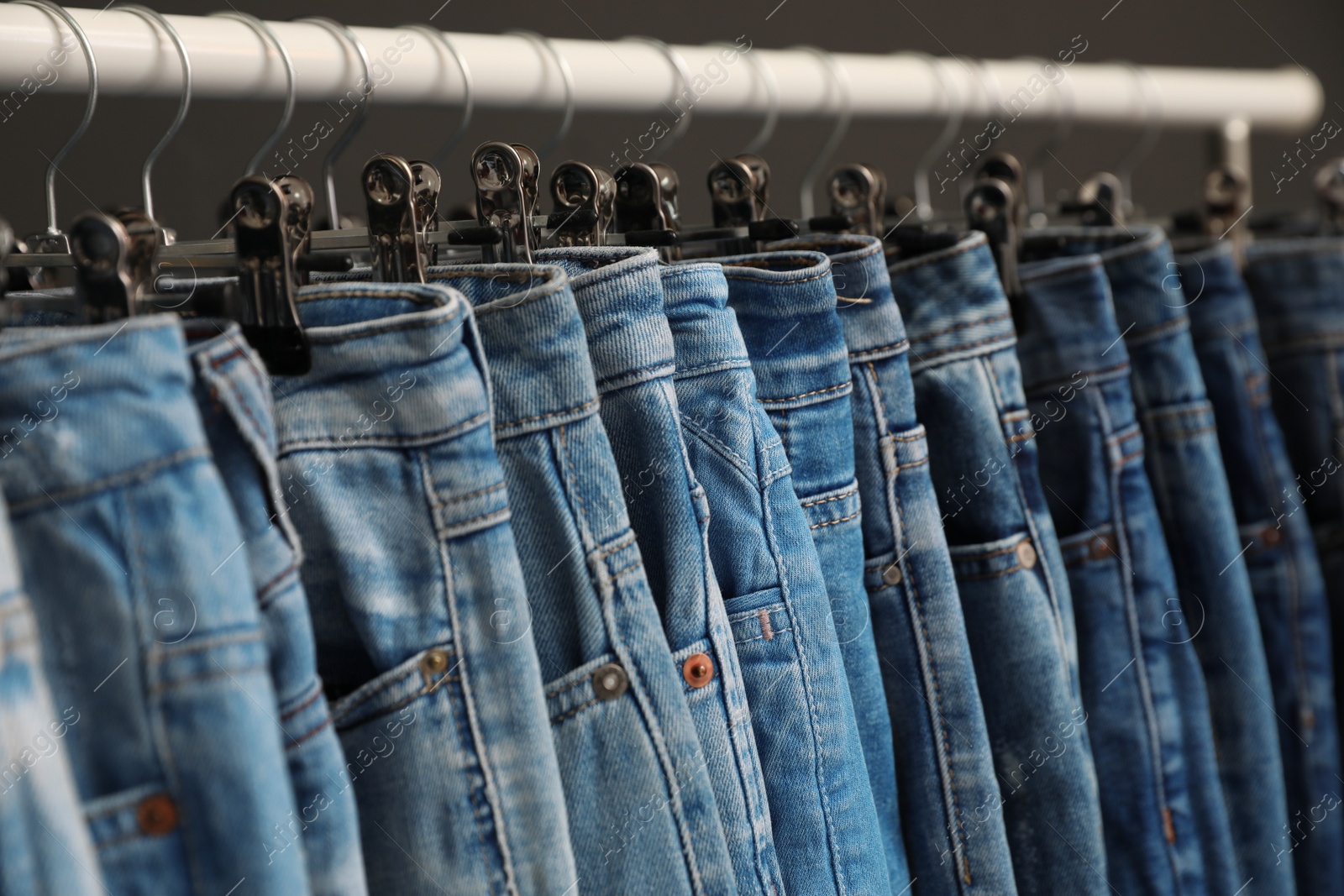 Photo of Rack with different jeans on dark grey background, closeup