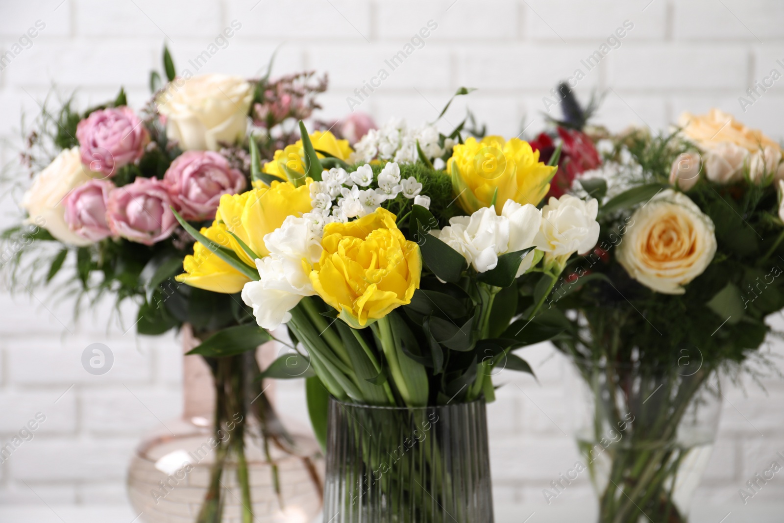 Photo of Beautiful bouquets with fresh flowers against white brick wall, closeup