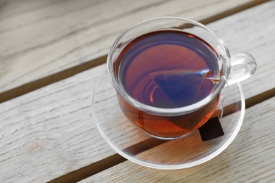 Bag of black tea in cup on wooden table
