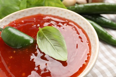 Photo of Spicy chili sauce with basil on table, closeup