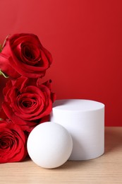 Photo of Stylish presentation for product. Beautiful roses and geometric figures on wooden table against red background