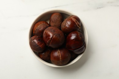 Roasted edible sweet chestnuts in bowl on white marble table, top view