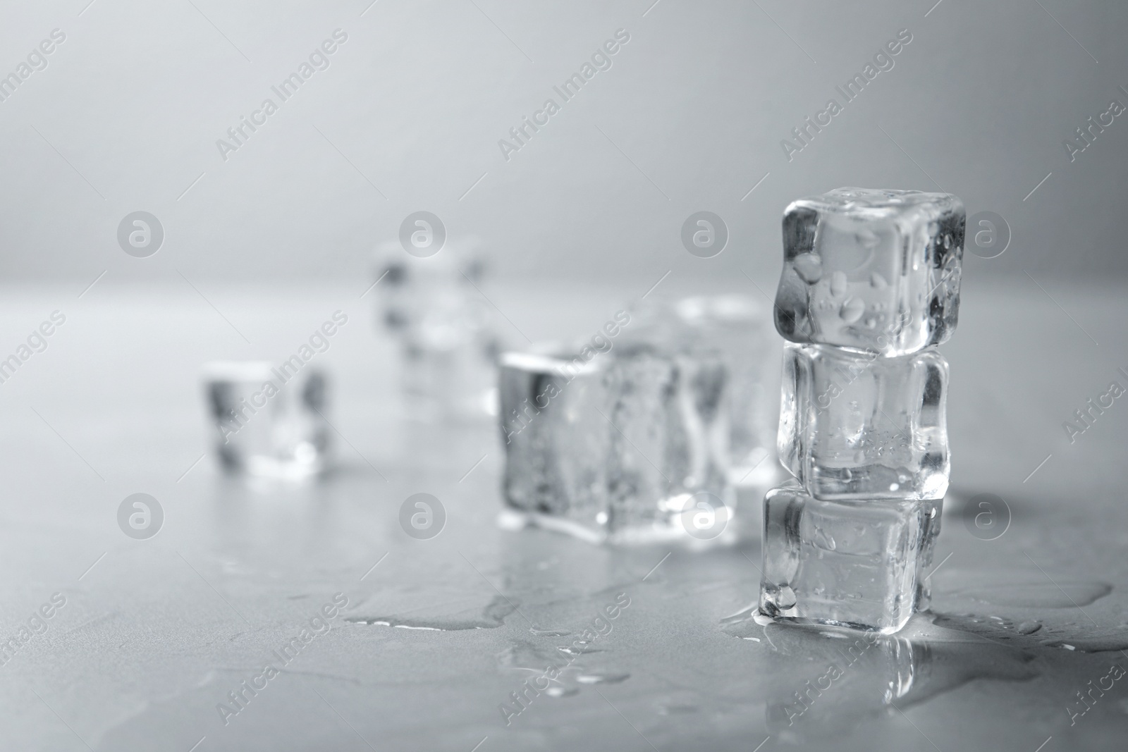 Photo of Crystal clear ice cubes with water drops on grey table. Space for text