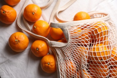 Photo of Net bag with many fresh ripe tangerines on white cloth, flat lay