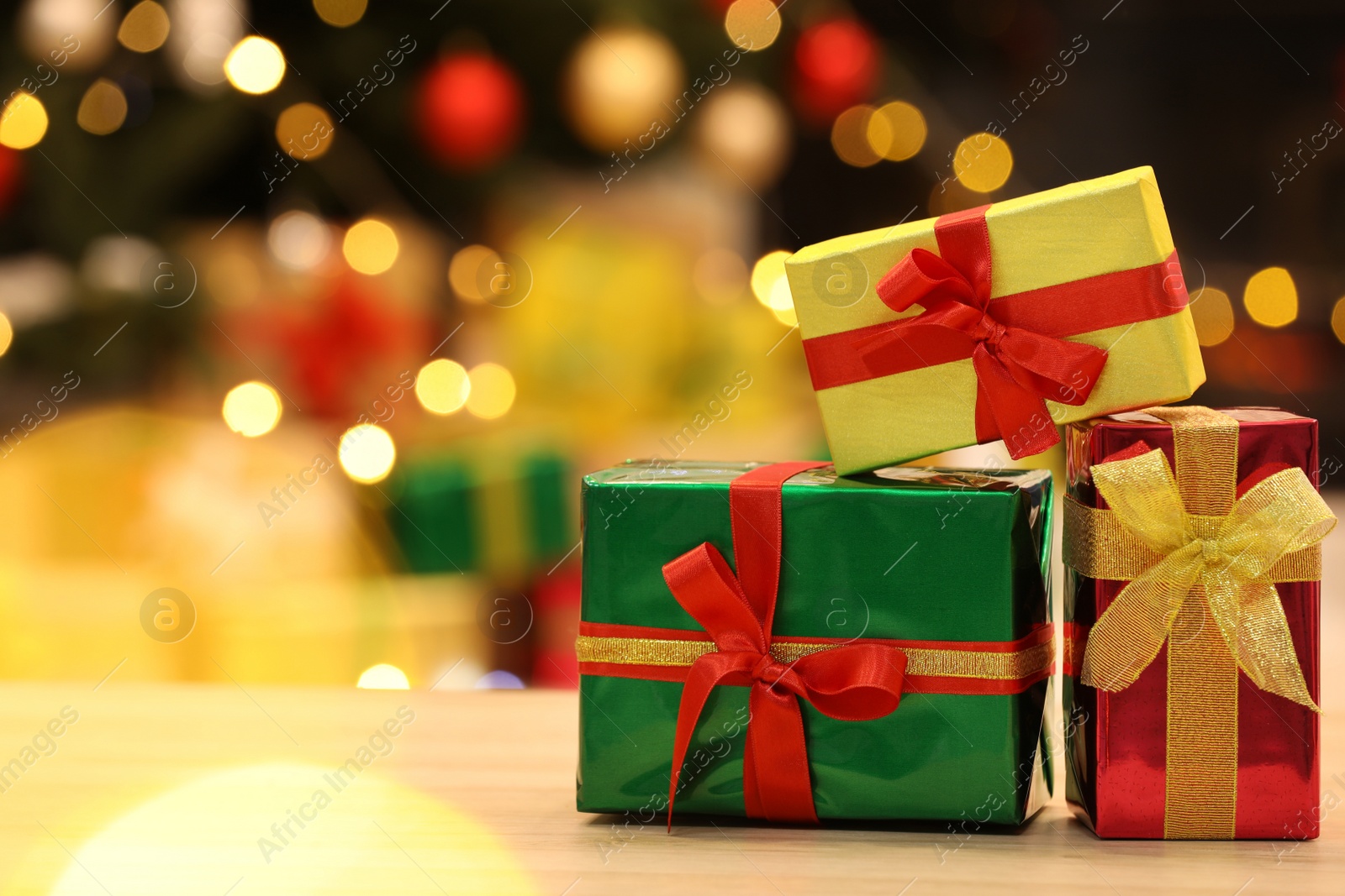 Photo of Beautifully wrapped gift boxes on wooden table against blurred festive lights, space for text. Christmas celebration