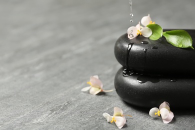 Pouring water onto spa stones with flowers and leaves on table. Space for text