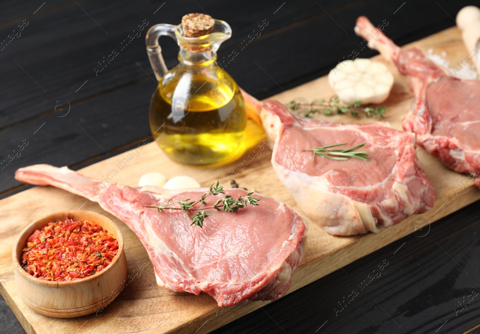 Photo of Fresh tomahawk beef cuts, spices and oil on black wooden table