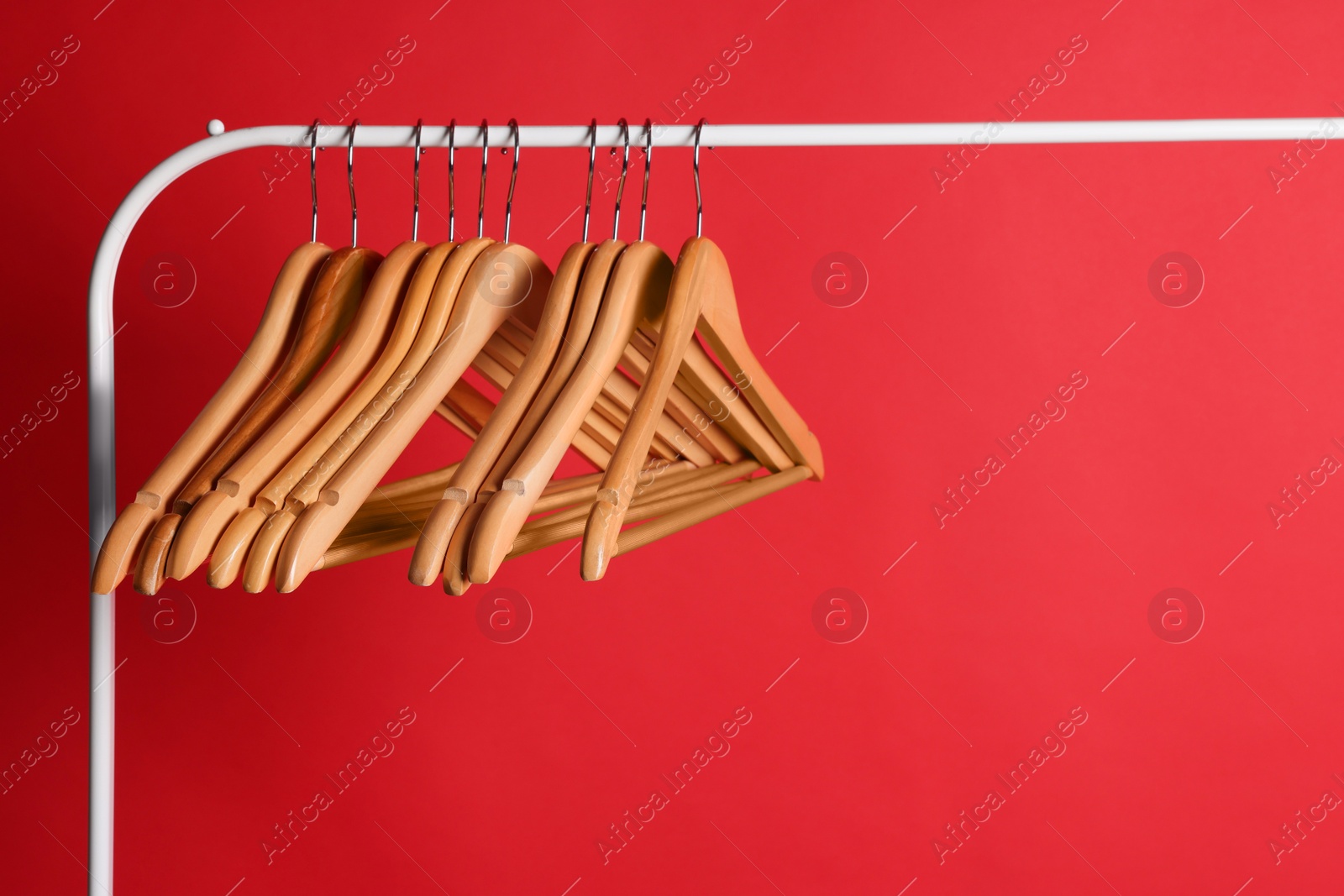 Photo of Wooden clothes hangers on metal rack against red background
