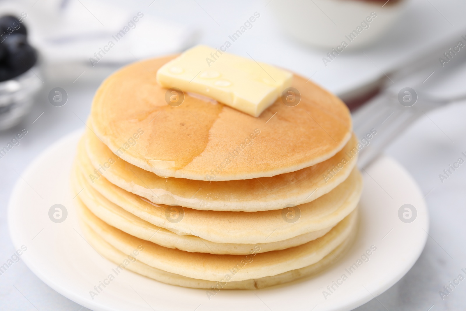 Photo of Delicious pancakes with butter and honey on white table, closeup