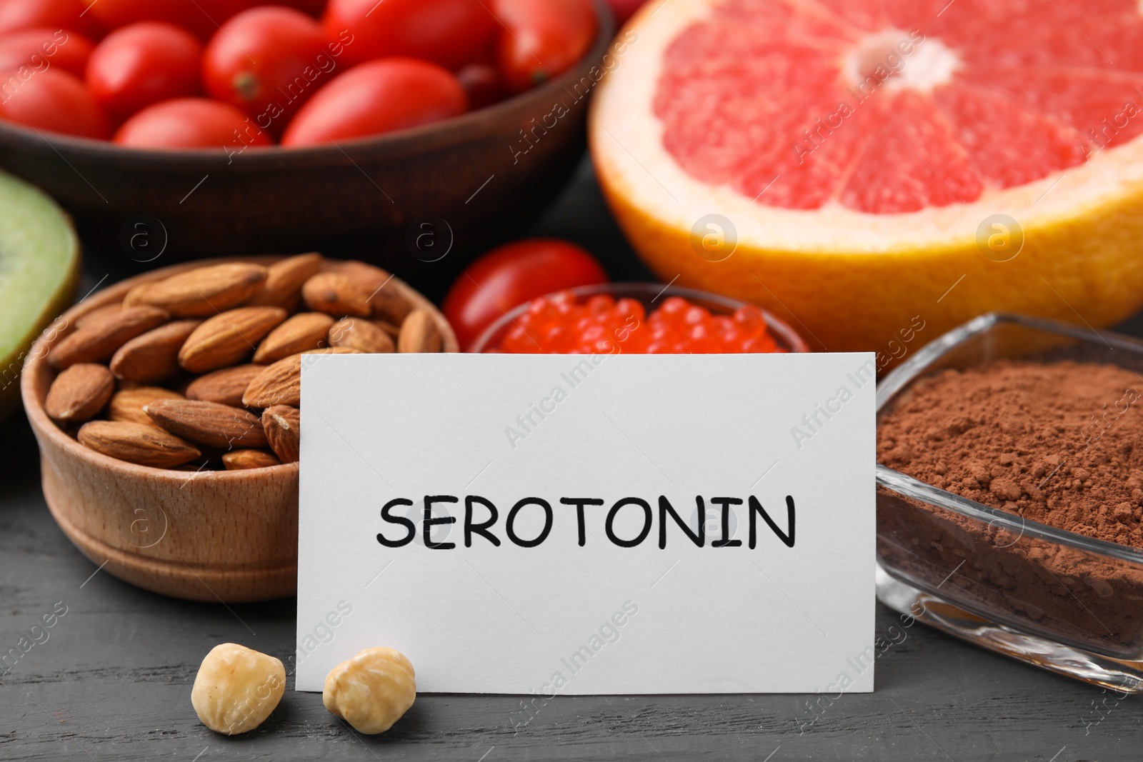 Photo of Many different products and card with word Serotonin on grey wooden table, closeup. Natural antidepressants