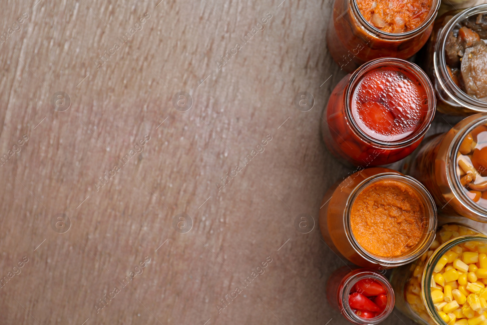 Photo of Flat lay composition with jars of pickled vegetables on brown table. Space for text