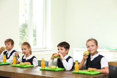 Happy children eating healthy food for lunch in school canteen