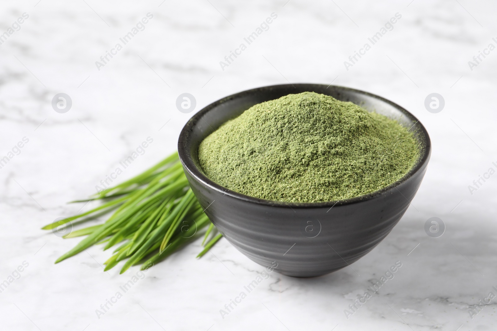 Photo of Wheat grass powder in bowl and fresh sprouts on white marble table, closeup