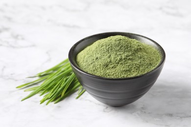 Wheat grass powder in bowl and fresh sprouts on white marble table, closeup